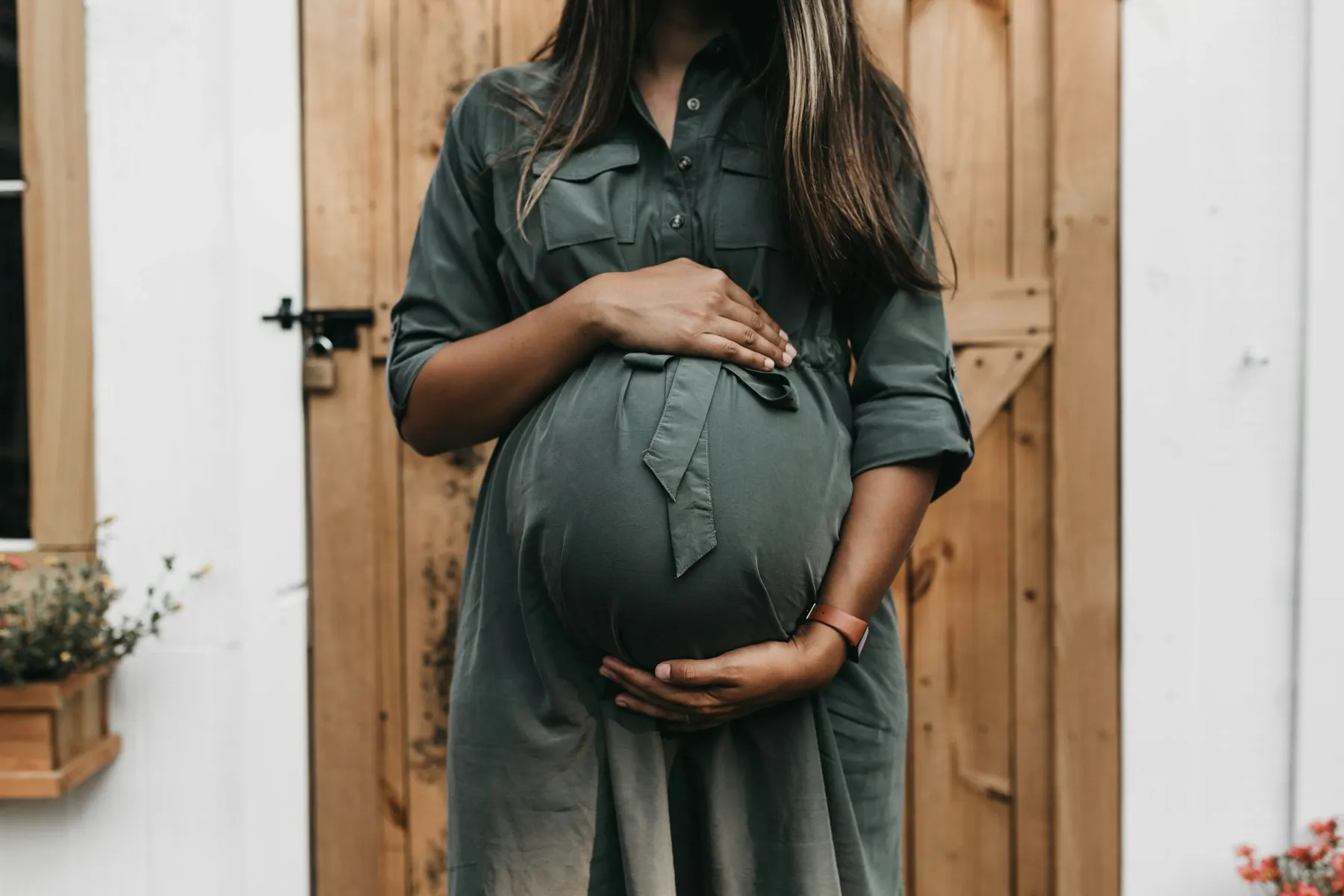 A pregnant woman in a green dress resting her hands on her bump